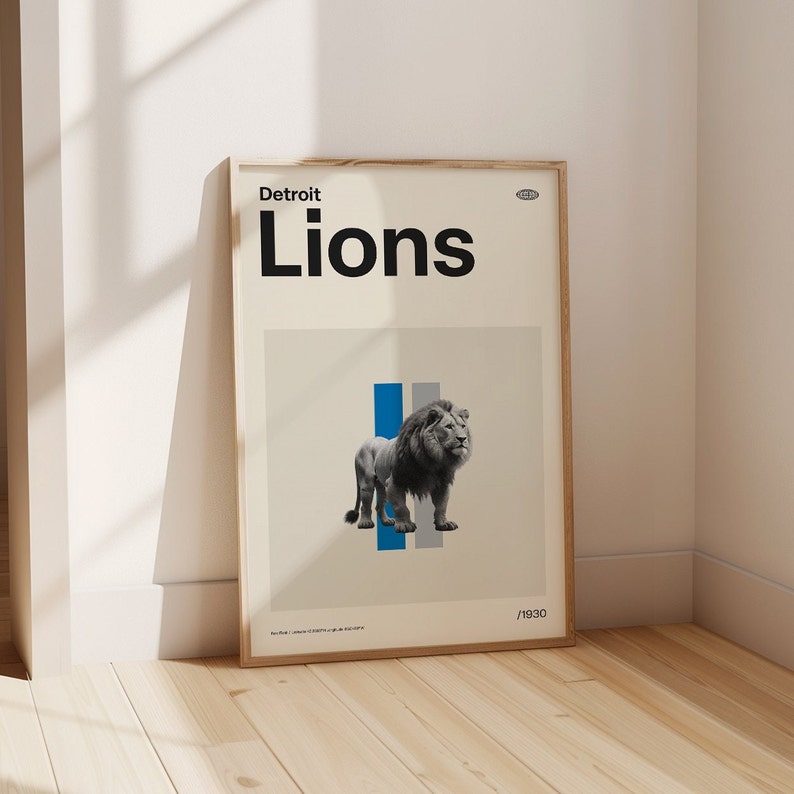 Op de afbeelding: Een ingelijste poster met een witte achtergrond en de tekst "Detroit Lions" in zwart. De poster toont een zwart-witte afbeelding van een leeuw die voor een blauwe en grijze streep staat.
