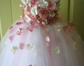 May include: A white tulle tutu dress with a pink and white flower bodice. The dress is decorated with pink and white flower petals.