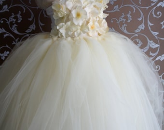 May include: A white tulle dress with a flower embellishment on the bodice. The dress is on a white mannequin.