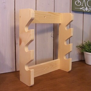 May include: A wooden wall-mounted stand with four hooks for hanging items. The stand is made of unfinished light wood and has a simple design.