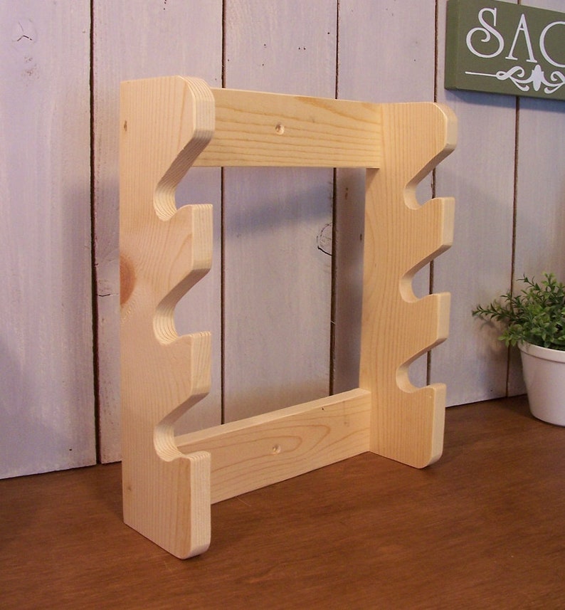 May include: A wooden wall-mounted stand with four hooks for hanging items. The stand is made of unfinished light wood and has a simple design.