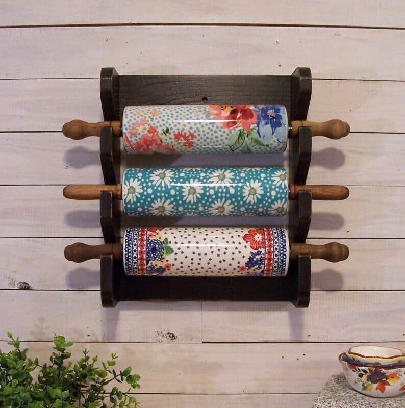 May include: A black wooden rolling pin rack with three ceramic rolling pins. The rolling pins have floral and polka dot patterns in shades of blue, white, and red.