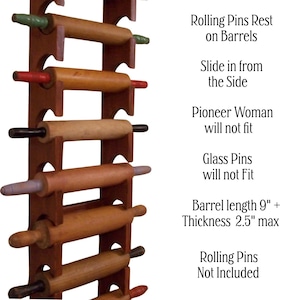 Op de afbeelding: Een bruin houten deegrollerrek met verschillende deegrollers. Het rek bevat deegrollers met verschillende handvatkleuren. De tekst luidt "Rolling Pins Rest on Barrels" en "Lengte cilinder 23 cm + Dikte 6,35 cm max".