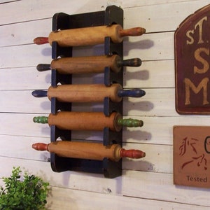 Peut inclure: Un porte-rouleaux en bois noir avec cinq rouleaux &agrave; p&acirc;tisserie en bois. Les rouleaux &agrave; p&acirc;tisserie ont des poign&eacute;es de diff&eacute;rentes couleurs, notamment rouge, bleu et vert. Le support est mont&eacute; sur un mur en bois blanc.