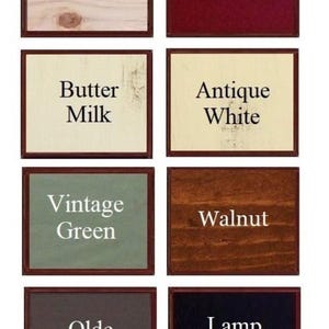 May include: A grid of eight rectangular wood colour samples with black text labels. The colours are Unfinished, Barn Red, Butter Milk, Antique White, Vintage Green, Walnut, Olde Gray, and Lamp Black. Each sample is framed in a thin dark brown border.