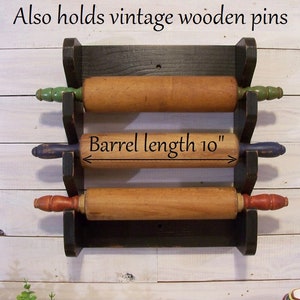 May include: Black wooden rolling pin rack with three rolling pins. The rack is mounted on a white wall. The middle rolling pin has a label that reads "Barrel length 10""