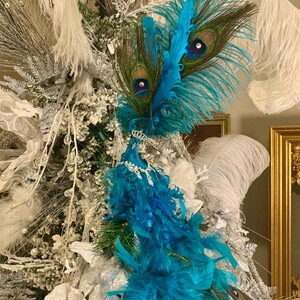 May include: A decorative peacock feather arrangement with vibrant turquoise and brown feathers, accented with sparkling embellishments. The arrangement is set against a backdrop of white and silver decorative elements, creating a festive and elegant display.