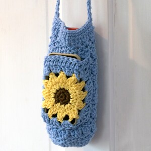 May include: A light blue crocheted bag with a sunflower design. The bag has a long strap and a pocket on the front.