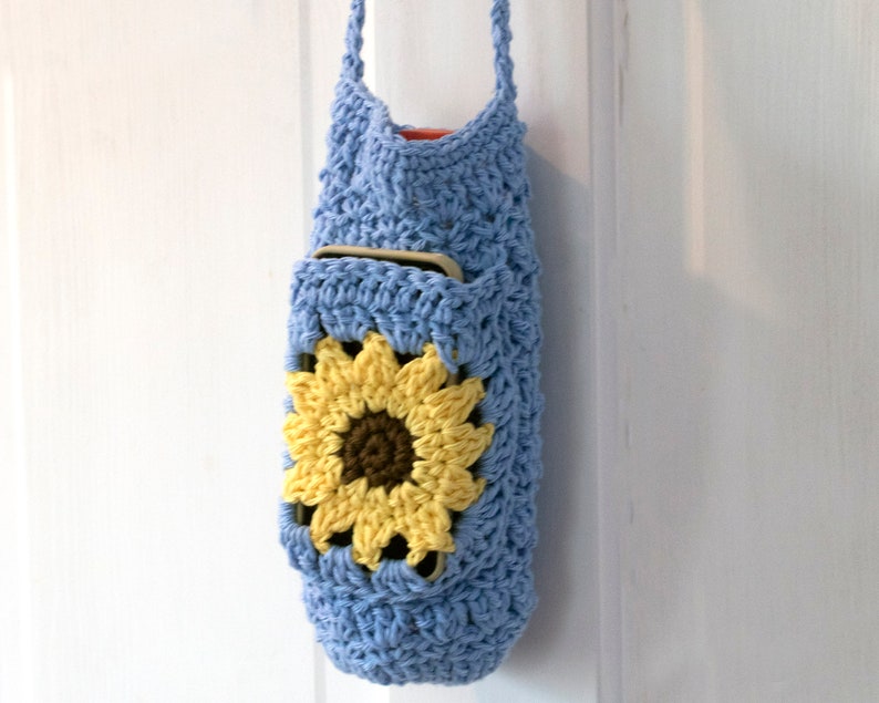 May include: A light blue crocheted bag with a sunflower design. The bag has a long strap and a pocket on the front.
