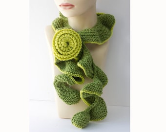 May include: A green and yellow knitted scarf with a large flower accent. The scarf is made of soft yarn and has a delicate, flowing design.
