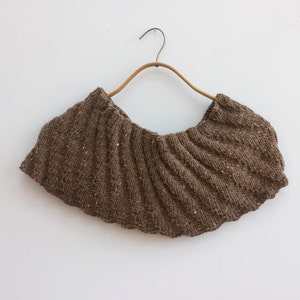 May include: A brown knitted cowl with a ruffled edge, hanging on a wooden hanger.