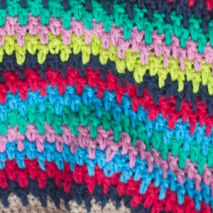 May include: Close-up of a colorful crocheted fabric with stripes of green, pink, blue, red, and black yarn.