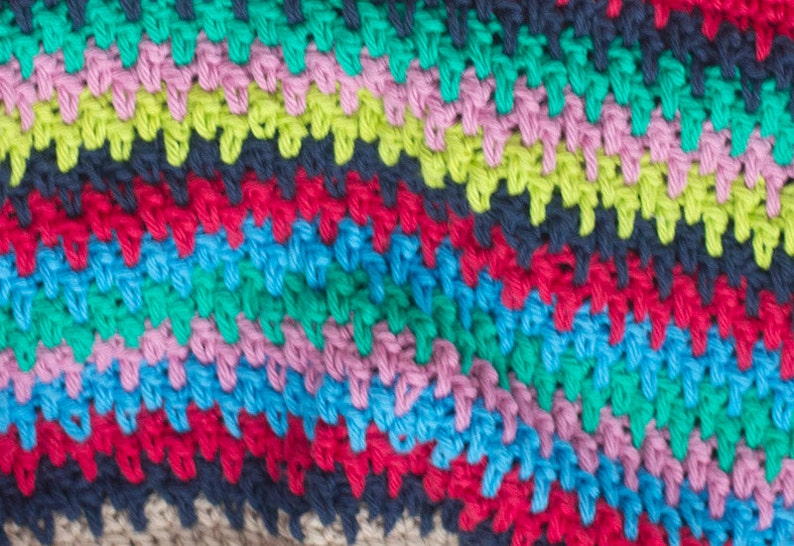 May include: Close-up of a colorful crocheted fabric with stripes of green, pink, blue, red, and black yarn.