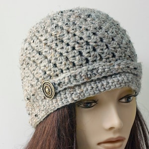 May include: A gray crocheted beanie with a button on the side. The beanie has a slouchy fit and a wide brim.