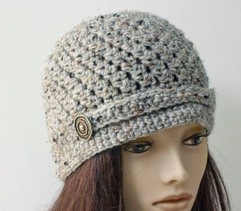 May include: A gray crocheted beanie with a button on the side. The beanie has a slouchy fit and a wide brim.
