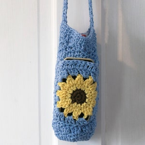 May include: A light blue crocheted bag with a sunflower design. The bag has a long strap and a pocket on the front.