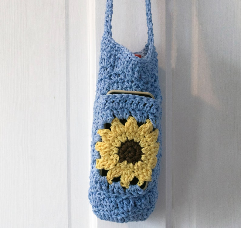 May include: A light blue crocheted bag with a sunflower design. The bag has a long strap and a pocket on the front.