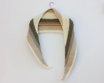 May include: A crocheted scarf in shades of beige, brown, and white, hanging on a wooden hanger.
