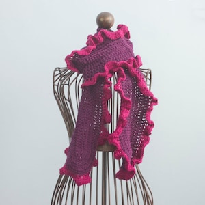 May include: A purple and pink crocheted scarf with a ruffled edge. The scarf is draped over a wire mannequin.