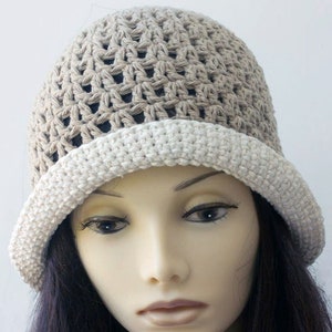 May include: A crocheted hat with a beige and white color gradient. The hat has a wide brim and a loose, open weave.