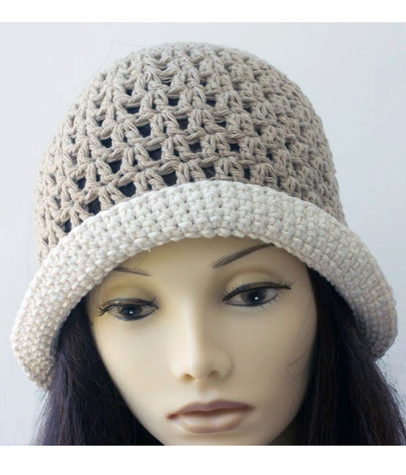 May include: A crocheted hat with a beige and white color gradient. The hat has a wide brim and a loose, open weave.