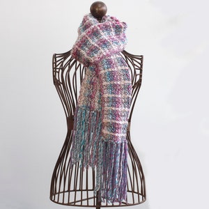 May include: A long, fringed scarf with a pink, white, and blue plaid pattern. The scarf is draped over a vintage-style metal dress form.
