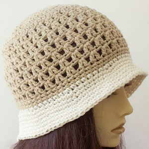 May include: A crocheted bucket hat with a beige and white color gradient. The hat is made with a loose, open stitch pattern.