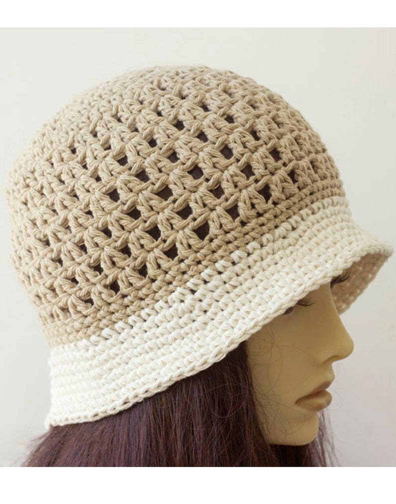 May include: A crocheted bucket hat with a beige and white color gradient. The hat is made with a loose, open stitch pattern.