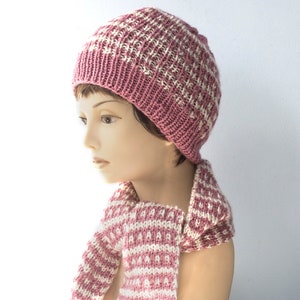 Puede incluir: Un gorro y una bufanda a juego de punto rosa y blanco con un patrón geométrico.