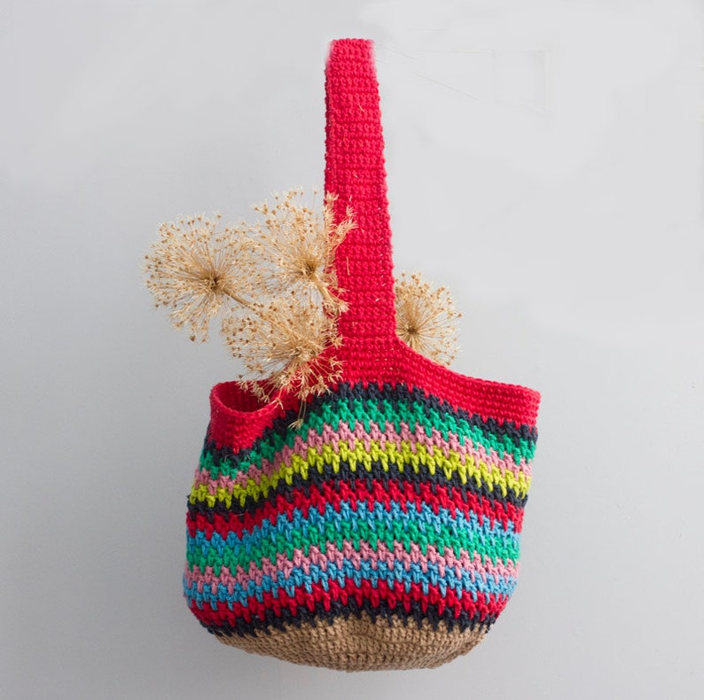 May include: A colorful striped crocheted tote bag with a red handle. The bag is filled with dried flowers.