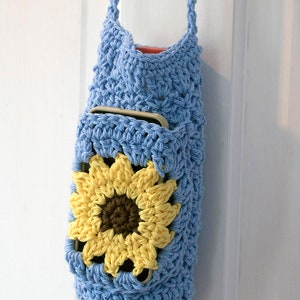 May include: A light blue crocheted bag with a sunflower design. The bag has a pocket on the front and a long strap.