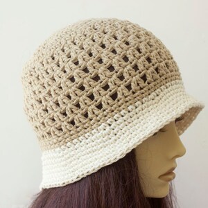 May include: A crocheted hat with a beige top and a white brim. The hat is made with a lacy stitch pattern.