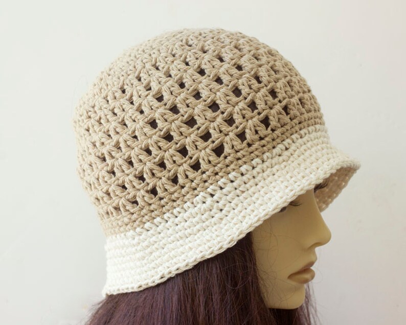 May include: A crocheted hat with a beige top and a white brim. The hat is made with a lacy stitch pattern.
