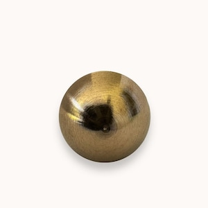 May include: A gold-colored metal sphere with a smooth, shiny surface. The sphere has a circular pattern on its surface.