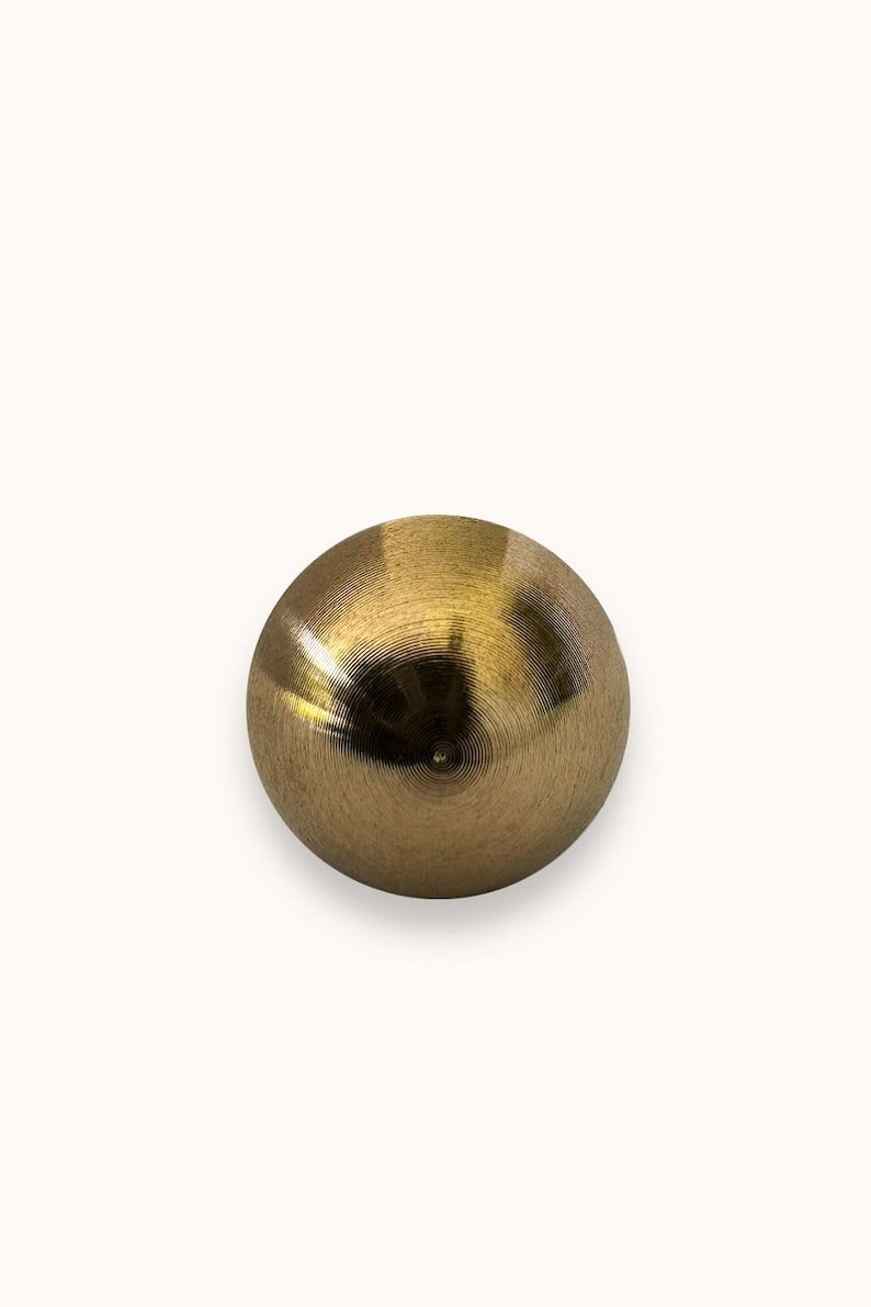 May include: A gold-colored metal sphere with a smooth, shiny surface. The sphere has a circular pattern on its surface.
