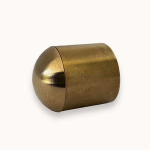 May include: A gold-colored metal end cap for a curtain rod. The end cap has a rounded, dome-shaped top and a cylindrical body.