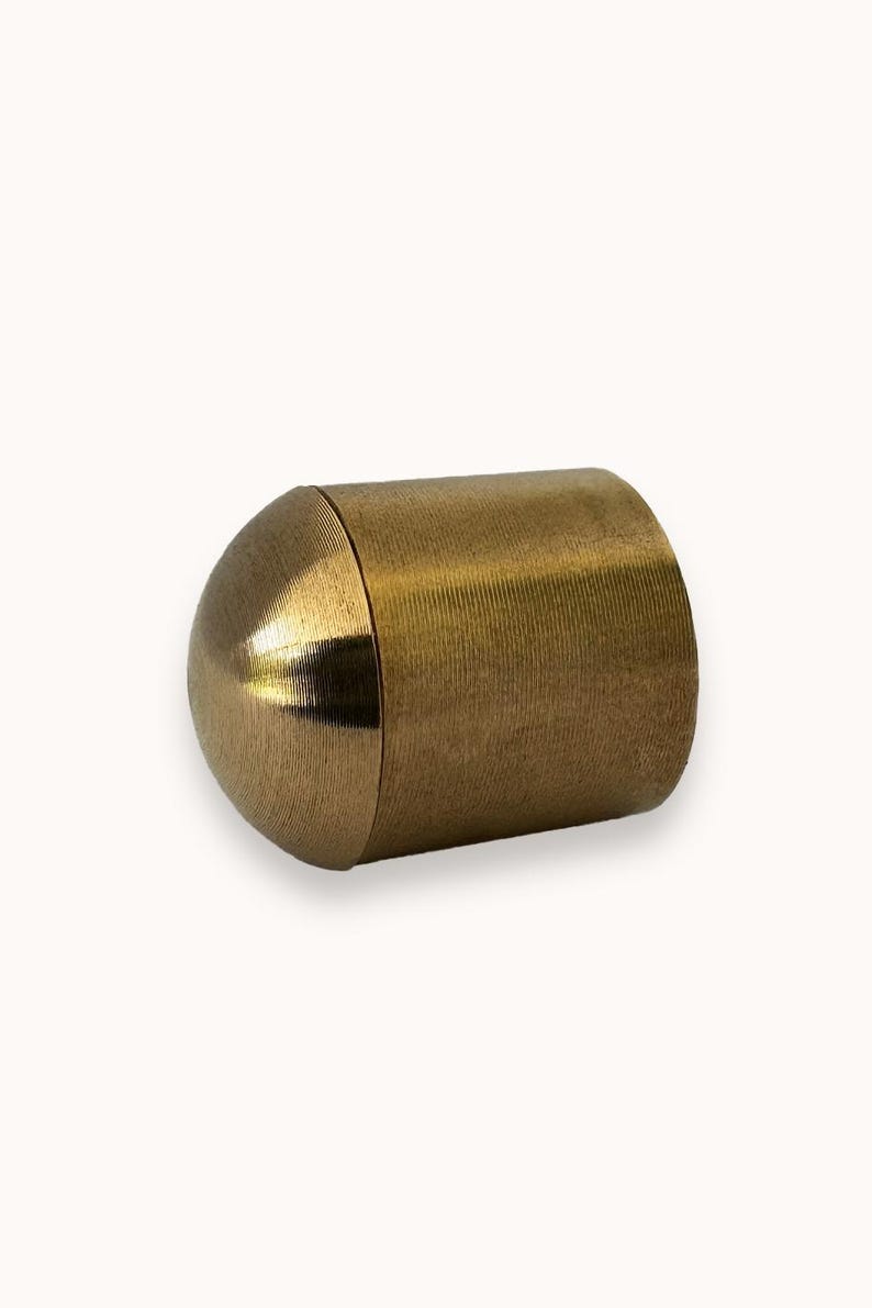 May include: A gold-colored metal end cap for a curtain rod. The end cap has a rounded, dome-shaped top and a cylindrical body.