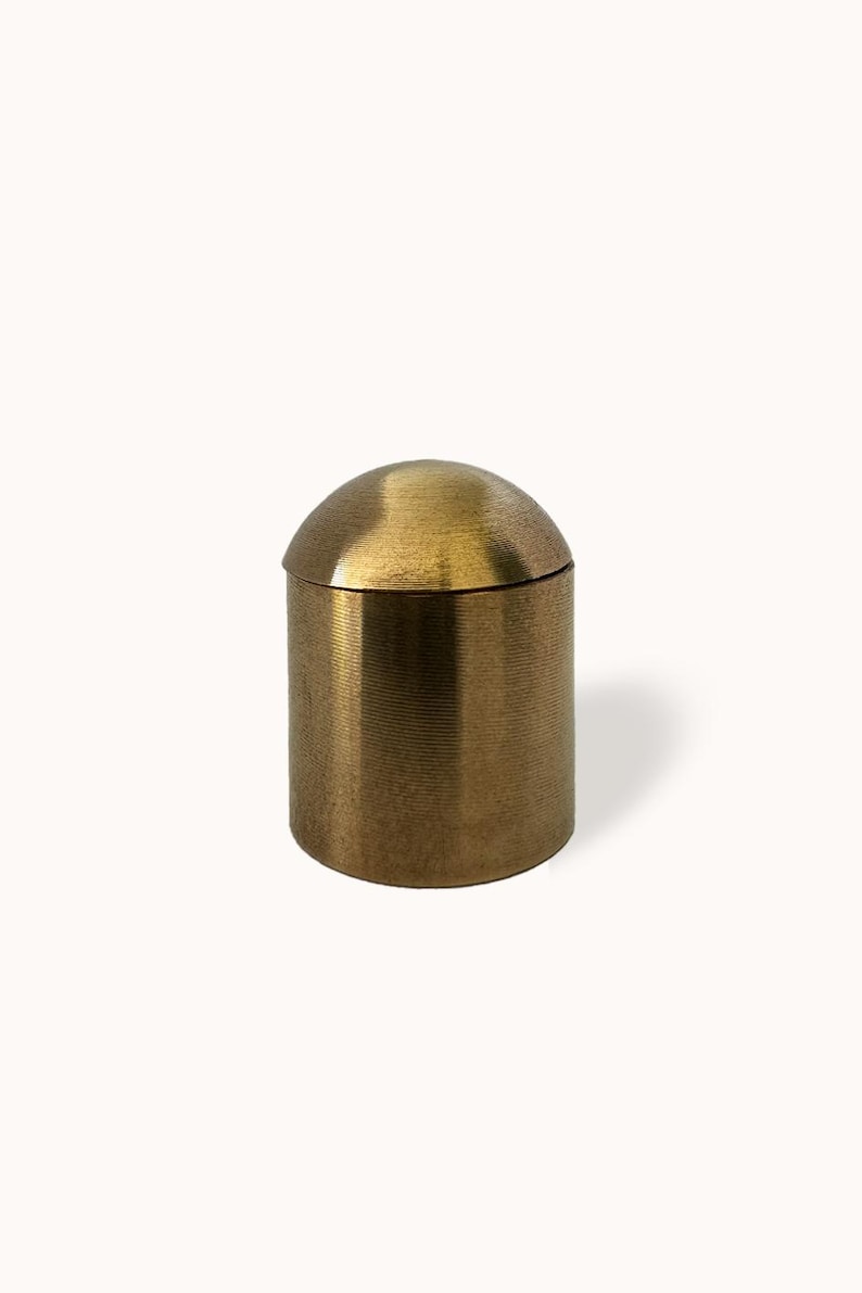 May include: A gold metal container with a domed lid. The container has a textured finish.