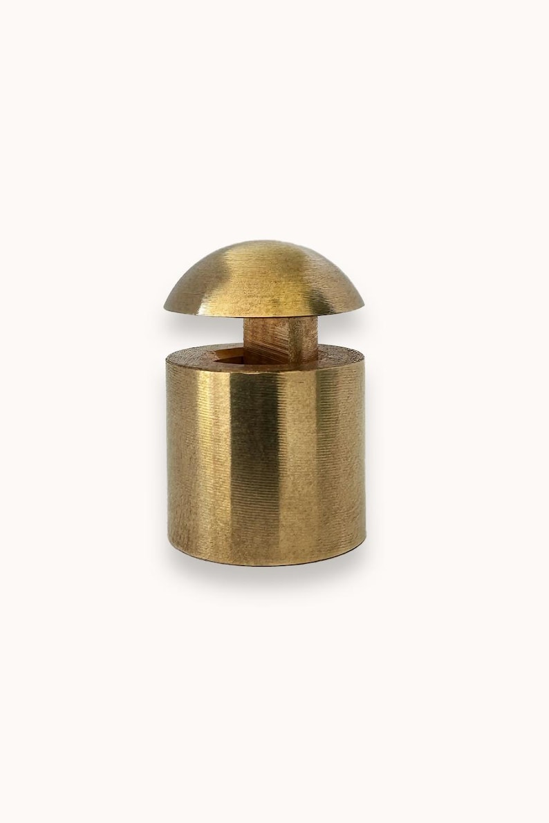 May include: A gold-toned metal bottle stopper with a dome-shaped top and a cylindrical base.