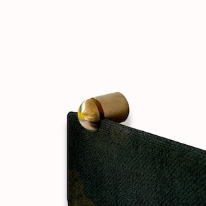 May include: A gold metal hook with a rounded top, attached to a black fabric surface.