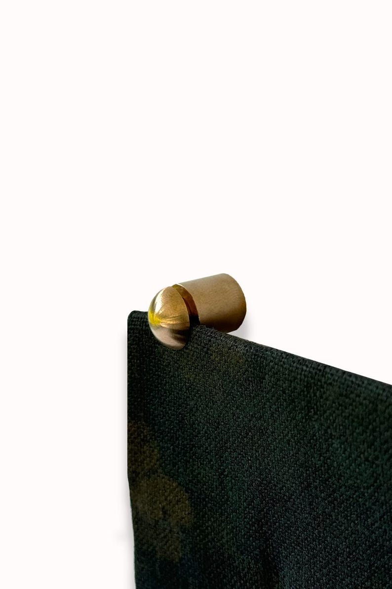 May include: A gold metal hook with a rounded top, attached to a black fabric surface.