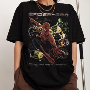 May include: Black Spider-Man t-shirt featuring a graphic of Spider-Man and the Green Goblin. The text "SPIDER-MAN" is at the top, and "WITH GREAT POWER COMES GREAT RESPONSIBILITY" is at the bottom.