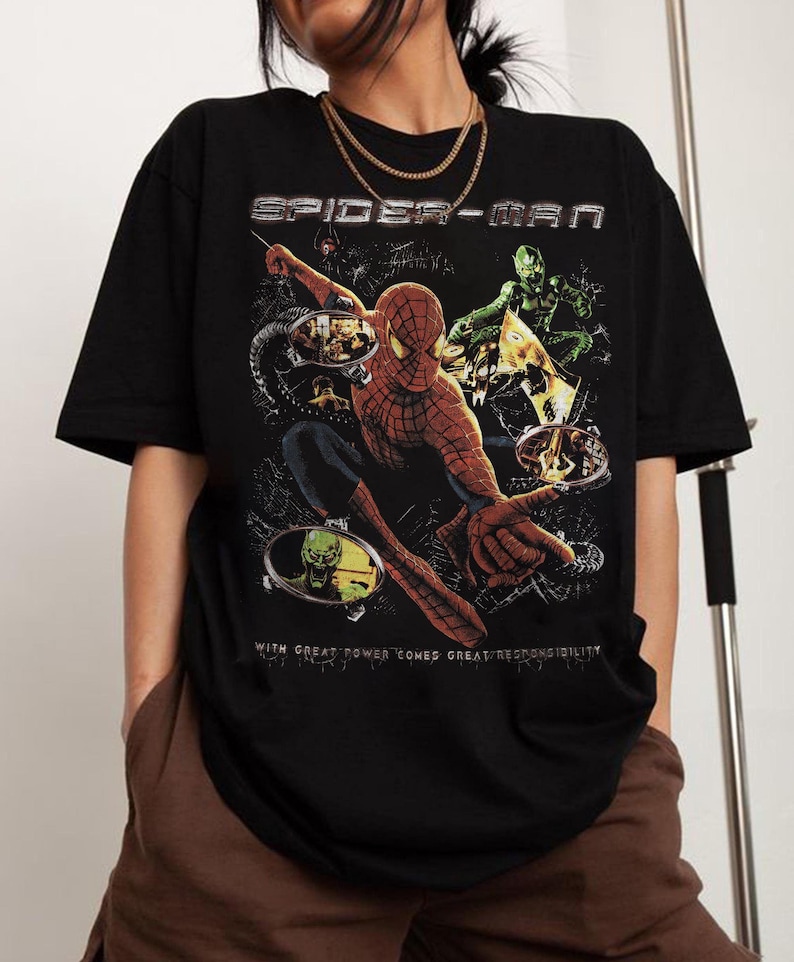May include: Black Spider-Man t-shirt featuring a graphic of Spider-Man and the Green Goblin. The text "SPIDER-MAN" is at the top, and "WITH GREAT POWER COMES GREAT RESPONSIBILITY" is at the bottom.