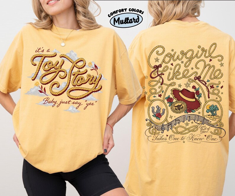 Może przedstawiać: Musztardowy t-shirt z grafiką z przodu przedstawiającą napis w stylu liny 'it's a Toy Story' oraz 'Baby, just say yes'. Z tyłu znajduje się napis 'Cowgirl like me' i 'Takes One to Know One' z ilustracjami kapelusza, liny oraz pustynnego krajobrazu.