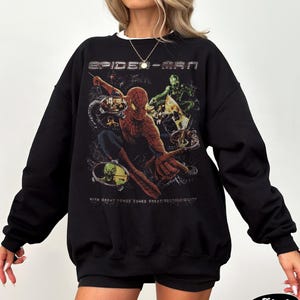 May include: Black Spider-Man sweatshirt featuring a graphic of the superhero in action with the text "SPIDER-MAN" above and "WITH GREAT POWER COMES GREAT RESPONSIBILITY" below. The sweatshirt has a crew neck and long sleeves.