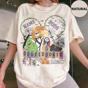 May include: A natural-colored t-shirt featuring a graphic print of characters from The Nightmare Before Christmas, including Jack Skellington, Sally, and Oogie Boogie. The design includes the text NAME, 2026, OOGIE BOOGIE, and BASH.