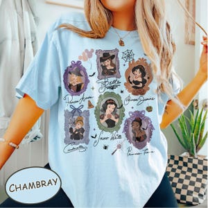 May include: Light blue t-shirt with a graphic featuring framed portraits of Disney princesses in Halloween costumes. The shirt includes the word "Chambray" and princess names in cursive script.