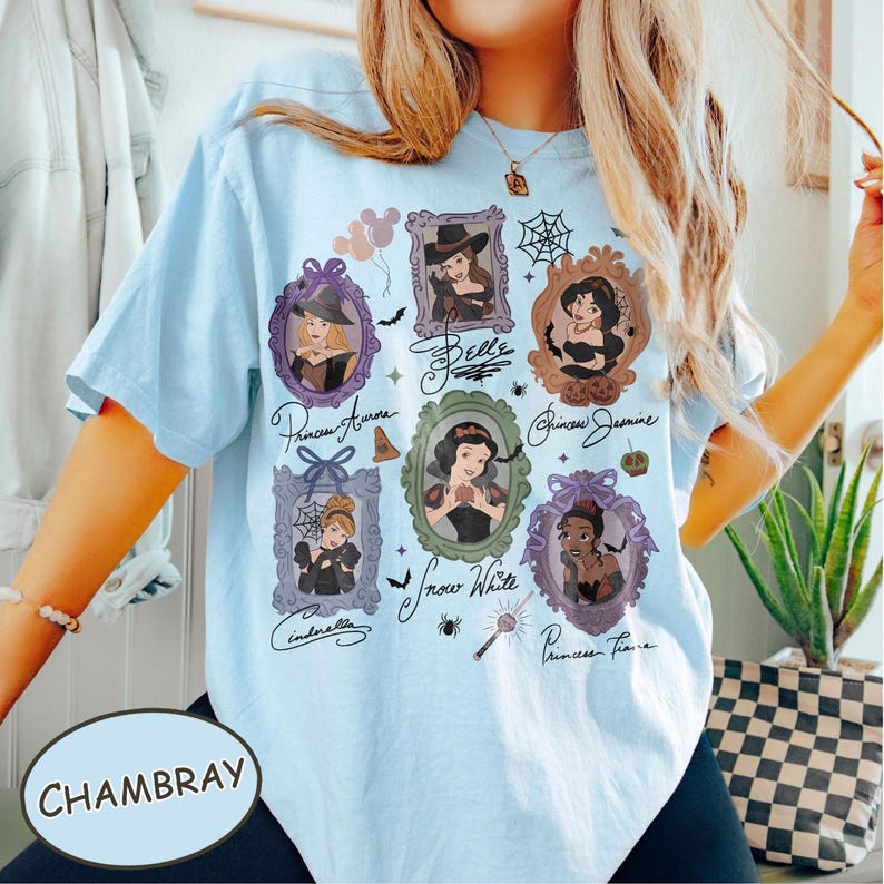 May include: Light blue t-shirt with a graphic featuring framed portraits of Disney princesses in Halloween costumes. The shirt includes the word "Chambray" and princess names in cursive script.