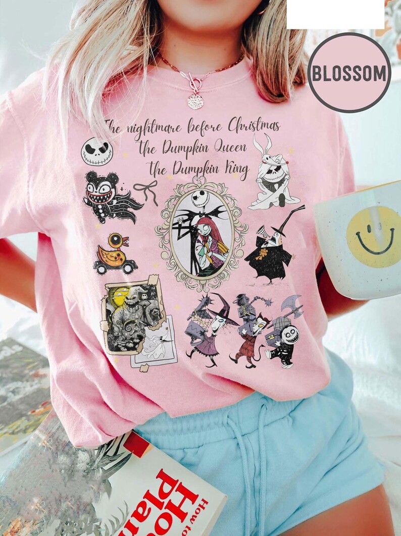 Pu&ograve; includere: T-shirt rosa chiaro con personaggi e testo di "Nightmare Before Christmas". Il design include Jack Skellington, Sally e altri personaggi. Il testo recita "The nightmare before Christmas, the Pumpkin Queen, The Pumpkin King."