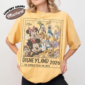 May include: Mustard-coloured t-shirt with a Disneyland 2026 graphic featuring Mickey Mouse, Minnie Mouse, Donald Duck, Goofy, and other Disney characters. The shirt has a vintage look with the words "Comfort Colors" above.
